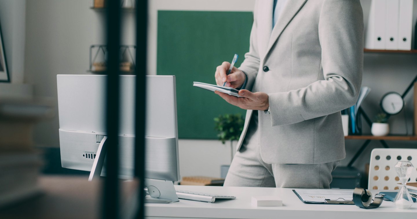 Persona in abito grigio che prende appunti alla scrivania in ufficio.