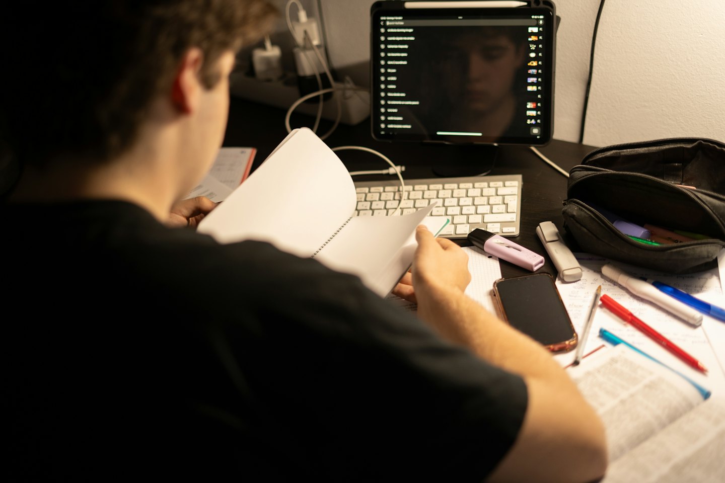 Persona che studia a una scrivania con taccuino e materiale.